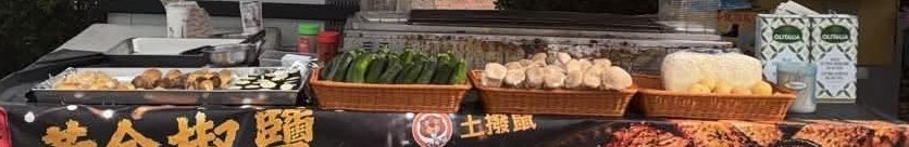 攤台上一籃籃新鮮櫛瓜與菇類，旁邊放著奧利塔橄欖油