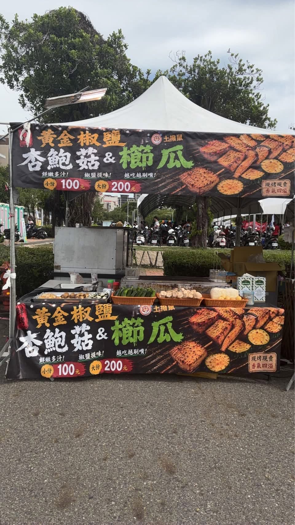 土撥鼠攤位全景：黑底金字帆布招牌，寫著黃金椒鹽杏鮑菇與櫛瓜